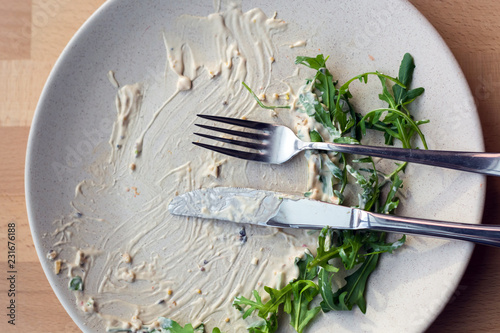 white plate with the remnants of the sauce and greens, on which lie a knife and fork