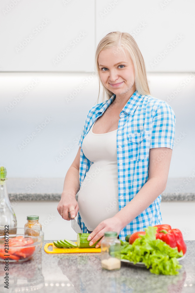 Smiling pregnant woman at kitchen prepares a vegetable salad