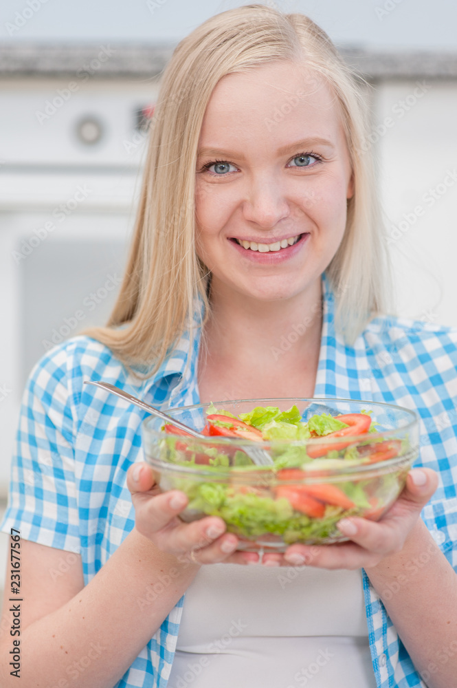 Happy blonde woman eating green healthy tasty eco salad at kitchen