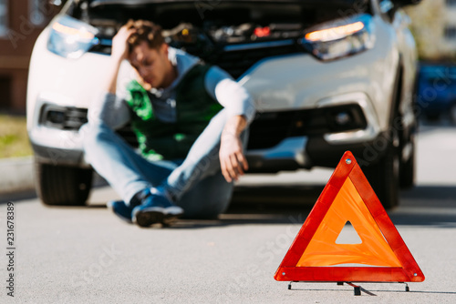 close-up view of road sign and upset man sitting near broken car on road