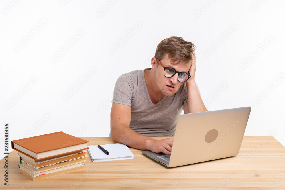 People and education concept - Puzzled student sitting at the wooden table with laptop People and education concept - Puzzled student sitting at the wooden table with laptop