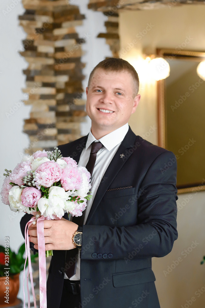 groom at wedding tuxedo smiling and waiting for bride in the hall of the hotel . Rich groom at wedding day. Elegant groom in costume and bow-tie. Groom in a suit holding buttonhole groom at wedding tuxedo smiling and waiting for bride in the hall of the hotel . Rich groom at wedding day. Elegant groom in costume and bow-tie. Groom in a suit holding buttonhole