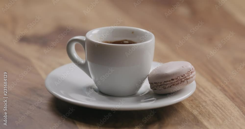 Slow motion man hand put beige macaron on saucer with coffee cup