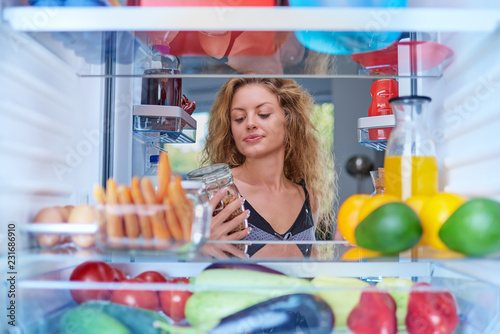 Woman taking jar from fridge full of groceries ato make a breakfast. Picture taken from the inside of fridge.