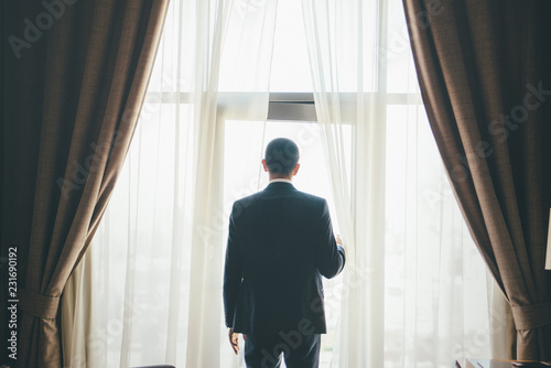 Groom is standing in front of curtained window