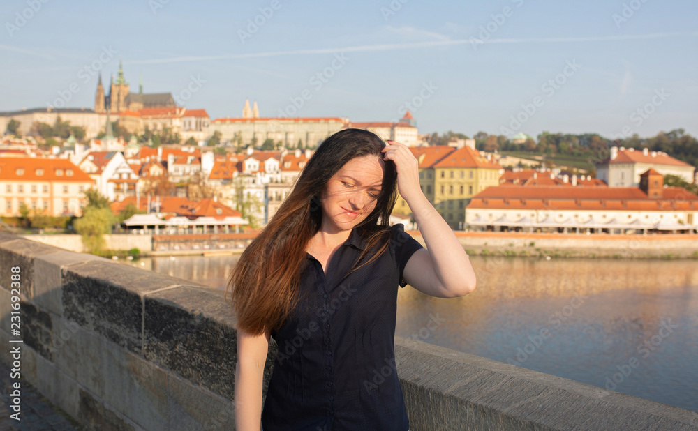 Street portrait of pretty brunette lady with long hair posing at the bridge in Prague