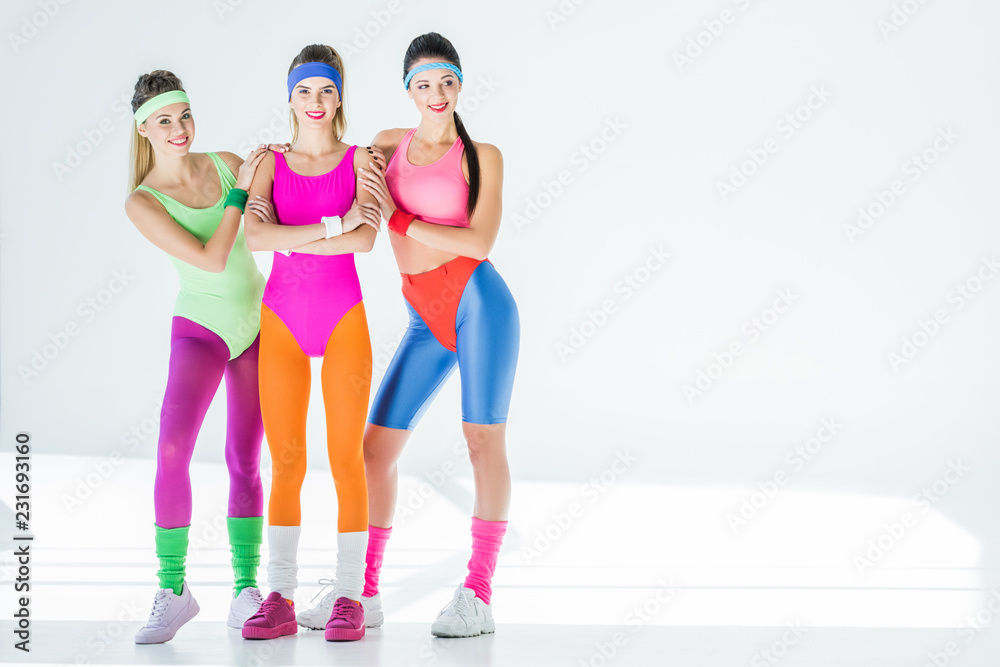 beautiful sporty young women in 80s style sportswear smiling at camera on  grey Stock Photo