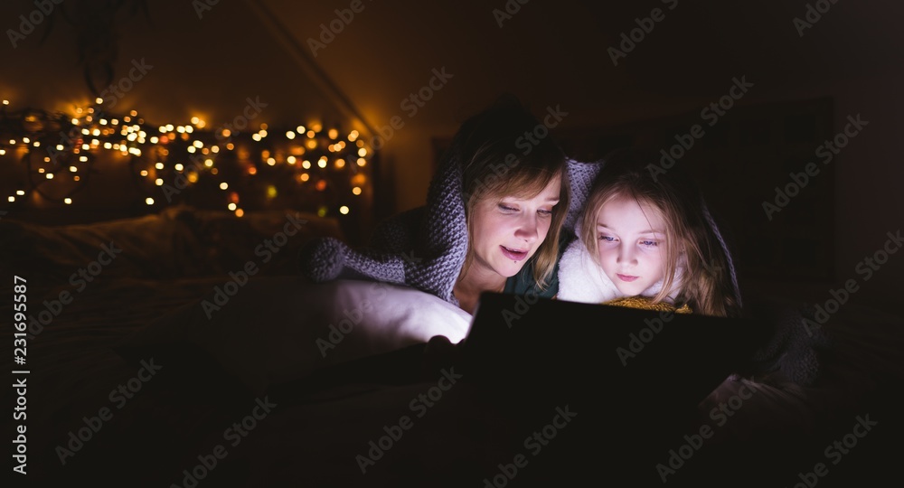 Mother and daughter under the blanket using digital tablet Mother and daughter under the blanket using digital tablet