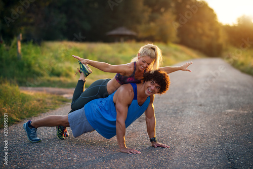 Training together is more fun. Young handsome man doing push ups while his girlfriend is sitting on his back.