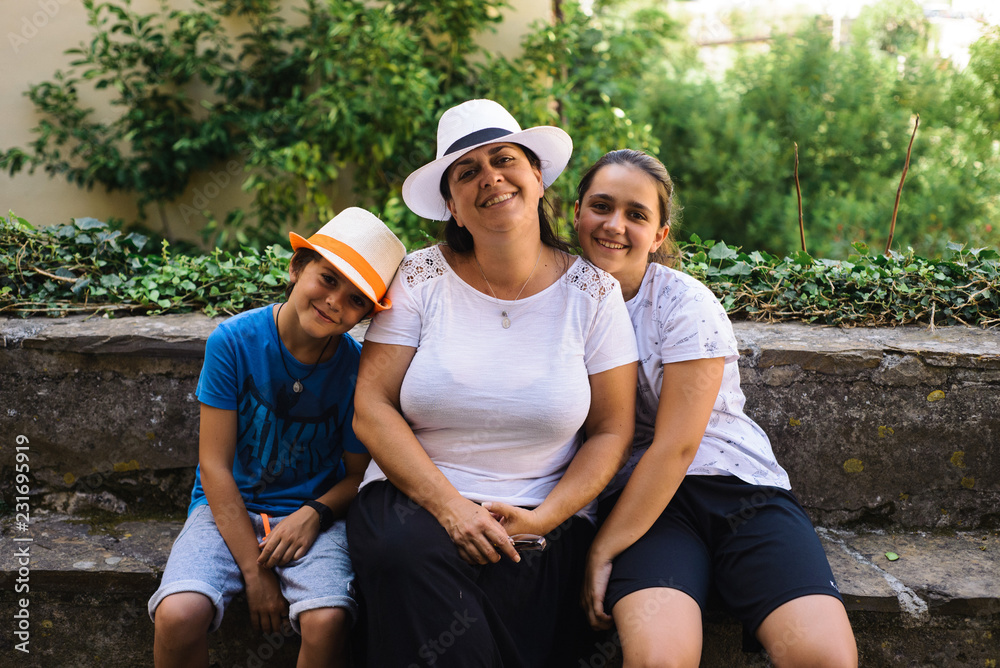 portrait of family mum with her children sitting on a low wall in Italy portrait of family mum with her children sitting on a low wall in Italy