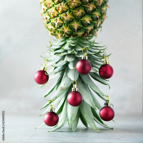 Creative Christmas tree made of pineapple and red bauble on grey concrete background, copy space. Greeting card, decoration for new year party. Holiday concept. Square crop