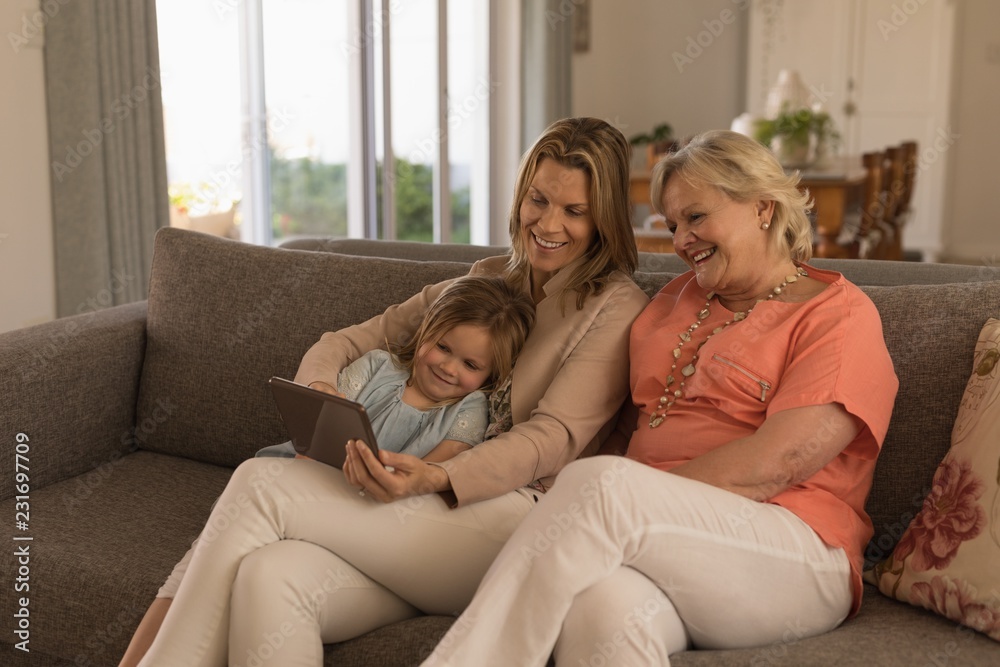 Multigenerational family using digital tablet while sitting on sofa in living room Multigenerational family using digital tablet while sitting on sofa in living room