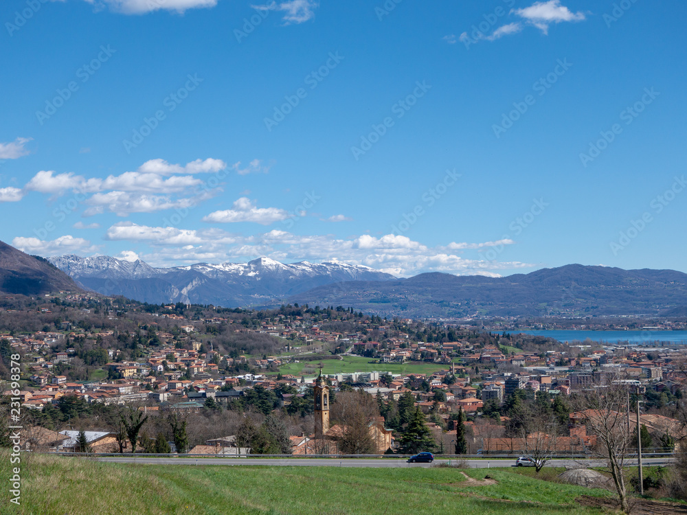 Panoramic view of the lake, mountains with snow and a small town. Alpine valley, Erba, Como, Lombardy, Italy