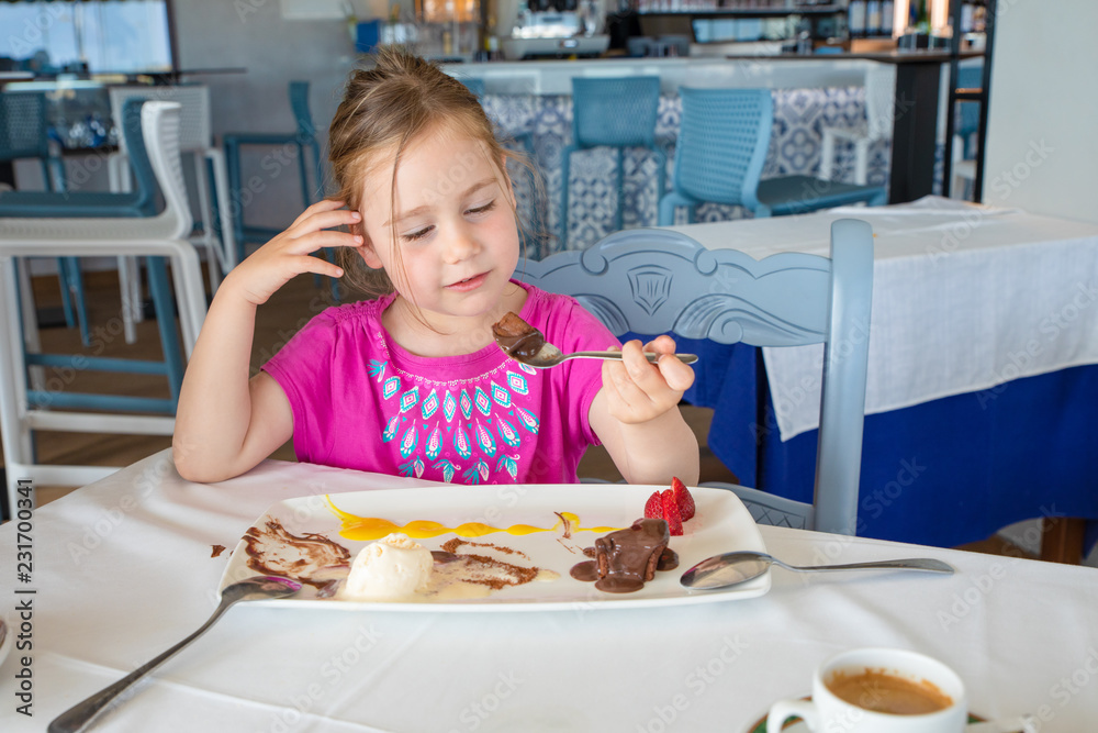 smiling little girl eating chocolate dessert in restaurant