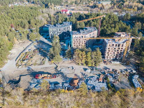 Aerial view of the construction of three elite residential buildings on the river bank in the middle of a green coniferous forest with a favorable environment, a lot of equipment costs near the site © Aleksandr Kondratov