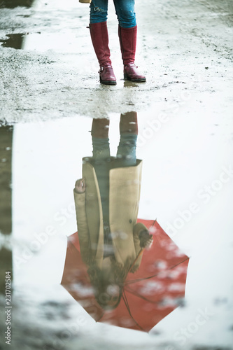 Reflection of a young woman with ubrella in the puddle