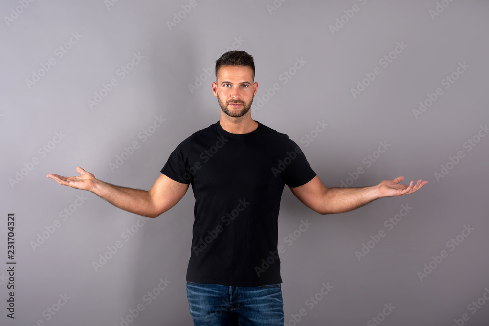 A handsome young man in a black tshirt showing something with his palms ...