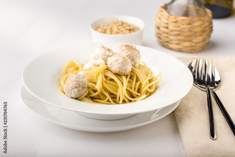 Spaghetti with creamy chicken meatballs served on white plate with pine nuts