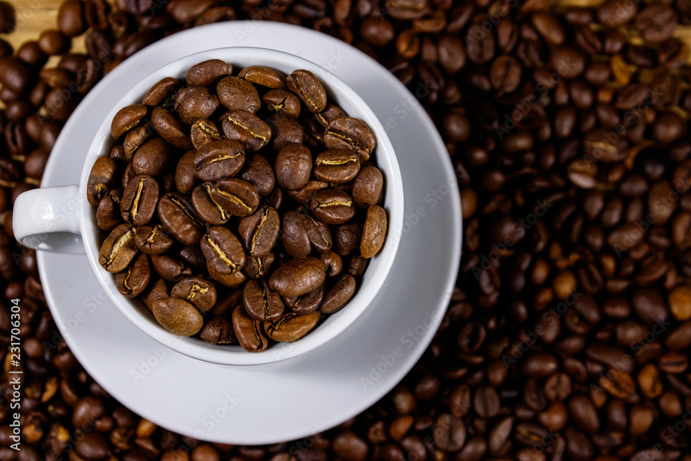 Roasted coffee beans in white cup on coffee beans background. Top view Roasted coffee beans in white cup on coffee beans background. Top view