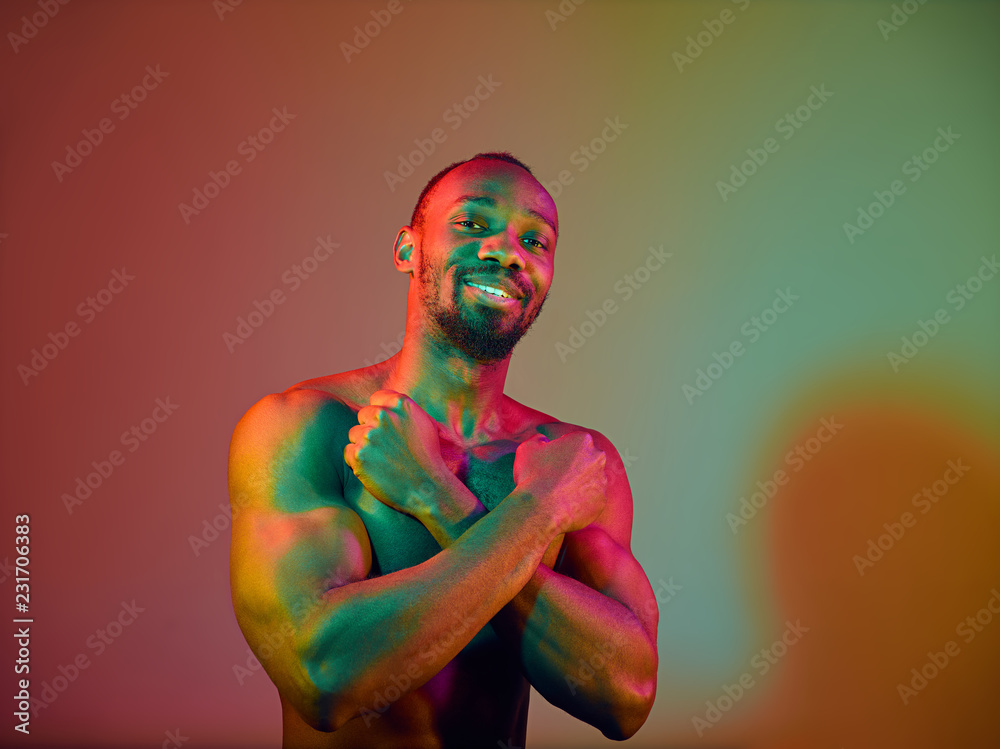 Close up portrait of a young naked happy smiling african man looking camera. High Fashion male model in colorful bright lights posing in studio. Art design over vivid background. Stock Photo
