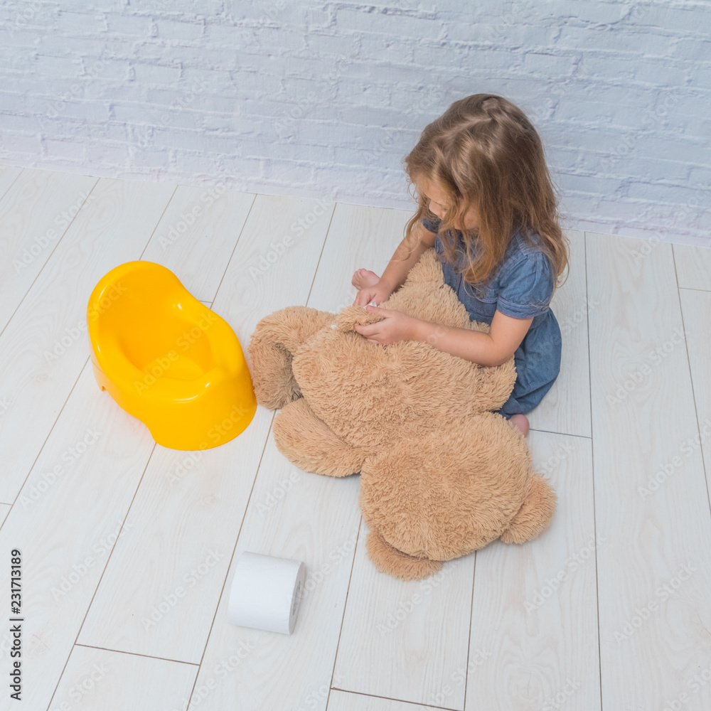 against the background of a white brick wall, the girl sits on a potty with the child, wiping ass with paper Stock-foto Adobe Stock