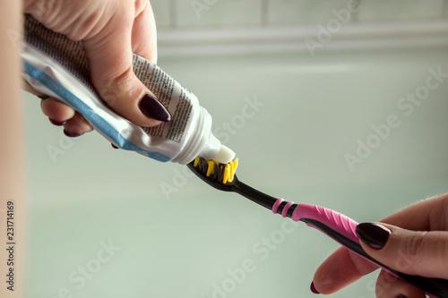 Woman hand holding toothbrush with toothpaste applied on it in bathroom. Close up of female hand ready for brushing teeth. Young woman hand holding a blue toothbrush with white tooth paste.