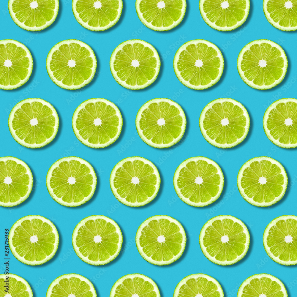Green lime slices pattern on vibrant turquoise color background. Minimal flat lay food texture 