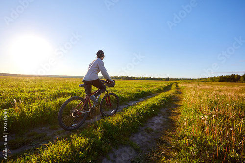 A young woman rides a bicycle on a field road. Summer sunny day