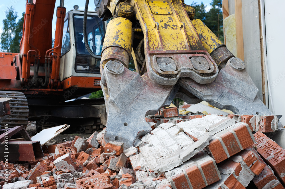 Demolition excavator crushing brick wall.