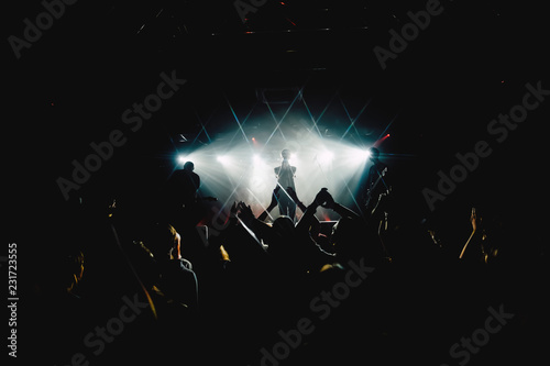 Singer applauding to the crowd of people at music concert with raised up hands. Rock band silhouette in a stage backlights