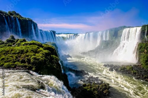 Water cascading over the Iguacu falls with rainbow in foreground in Brazil