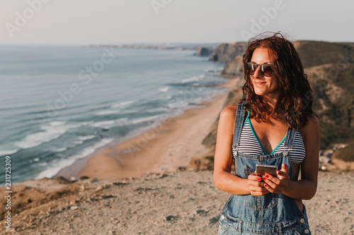 beautiful young woman on the top of a hill using her mobile phone and smiling. Summer time. Lifestyle