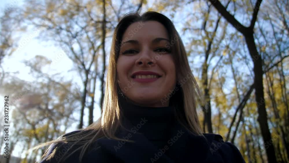 Portrait of a smiling woman circling in the autumn Park slow motion. 4k 60fps. Girl in a coat walking in the autumn city Park. Close up