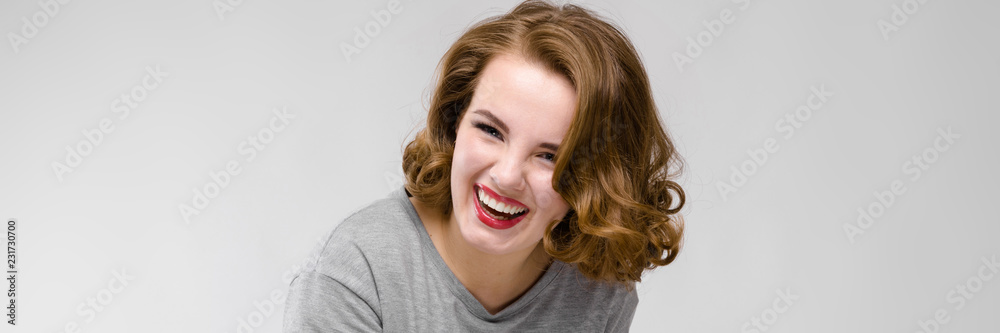Naklejka premium Charming young girl in a gray T-shirt on a gray background. The girl points with her finger and laughs