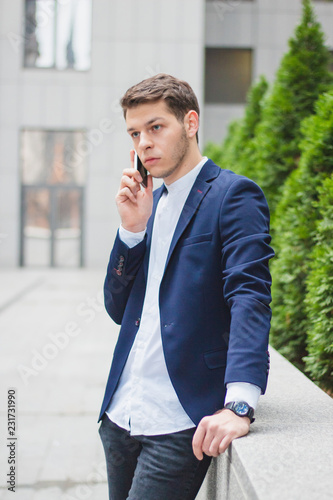 Business style. A young businessman is talking on the phone from the street. The guy in the blue jacket