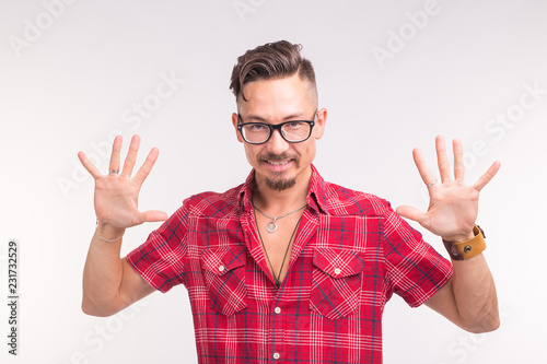 Emotions and people concept - handsome man showing you his hands or scares you, wearing checkered shirt and glasses on white background.