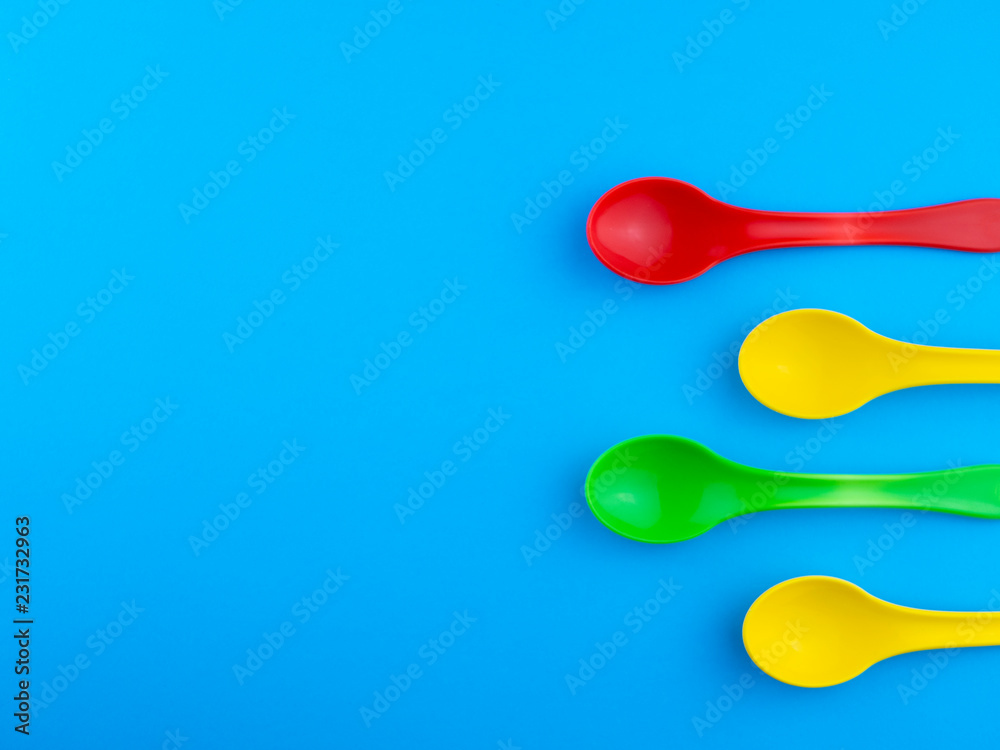 Yellow red and green plastic spoons on blue background with copy space for text Yellow red and green plastic spoons on blue background with copy space for text