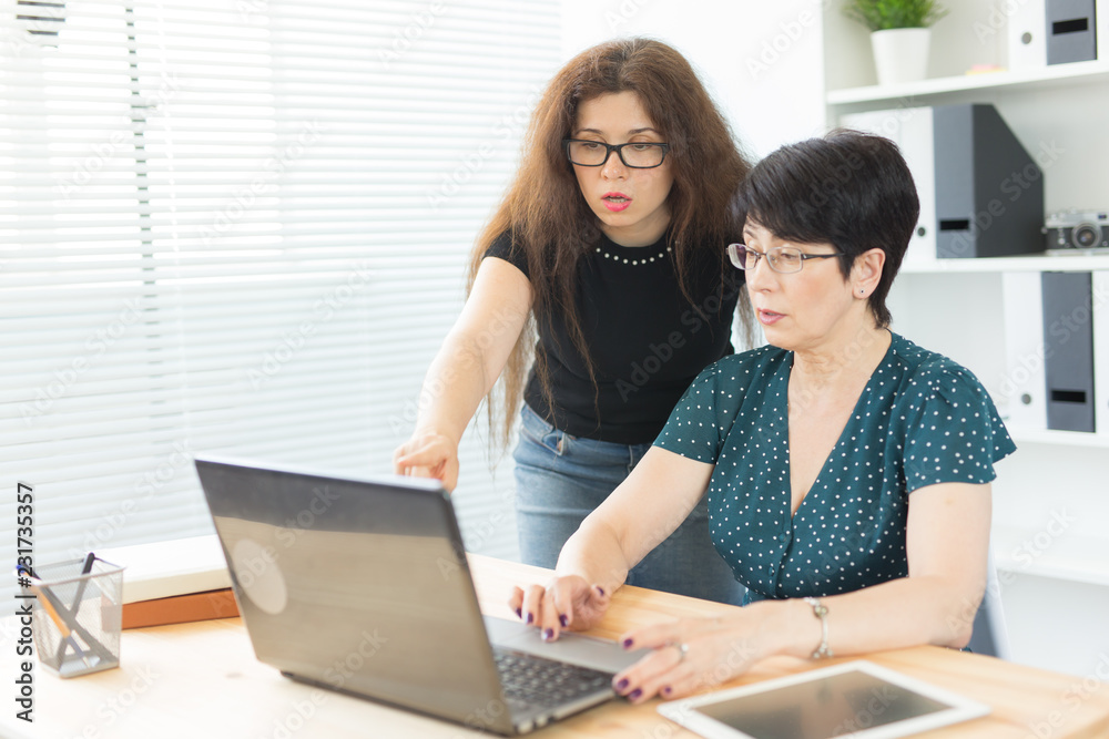 Business people, technology and communication concept - middle-aged woman showing something to another woman on laptop in office Business people, technology and communication concept - middle-aged woman showing something to another woman on laptop in office