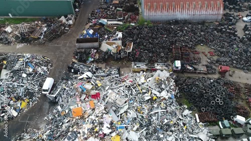 Aerial flight moving backwards over junkyard is the location of a business in dismantling where wrecked or decommissioned vehicles are brought showing pile of recyclable metal and old tires 4k quality photo