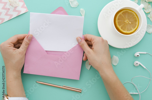 Woman drinking herbal tea. Hand holding a pink envelope with blank paper letter mockup on mint tiffany background. Top view flat lay message