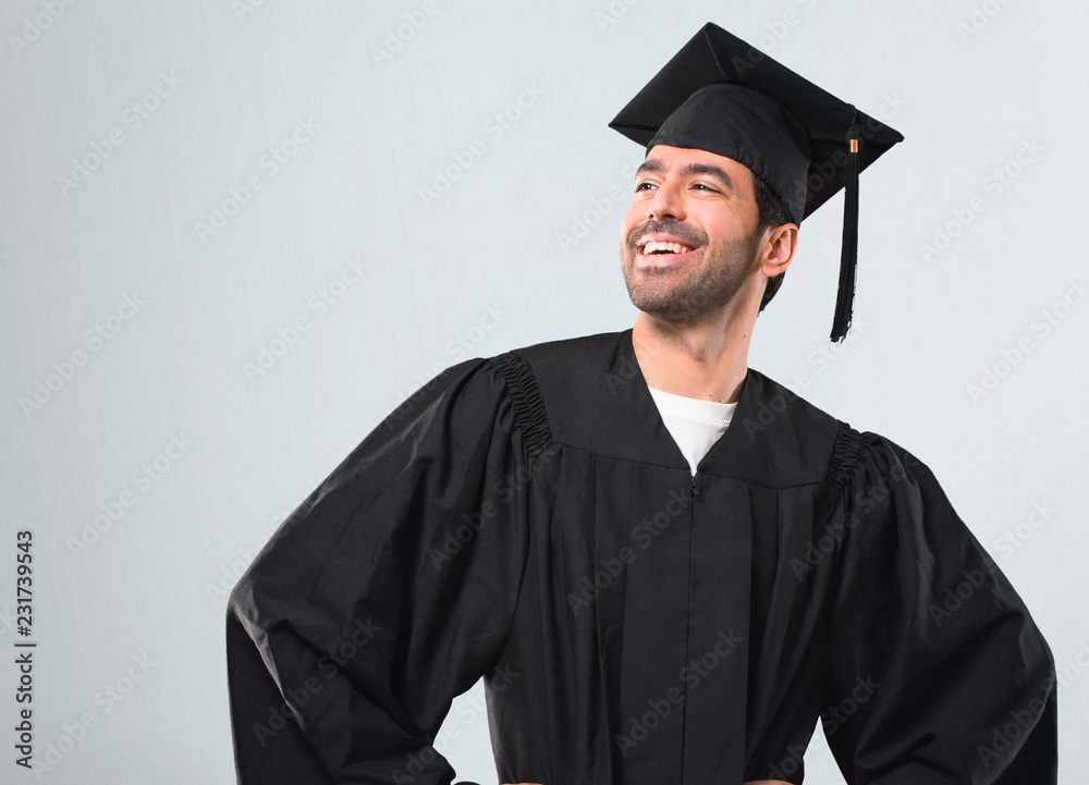 Man on his graduation day University posing with arms at hip and laughing on grey background Man on his graduation day University posing with arms at hip and laughing on grey background