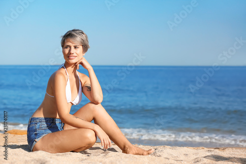 Young woman sitting on beach. Space for text