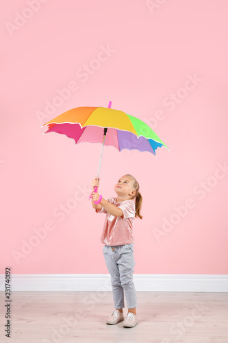 Little girl with rainbow umbrella near color wall