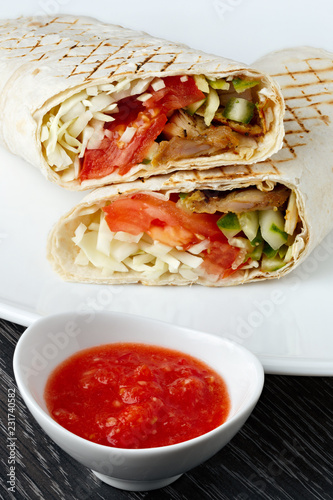 Shawarma in pita bread is cut and lies on a white plate. The Middle Eastern dish is prepared on the grill and served with sauce.