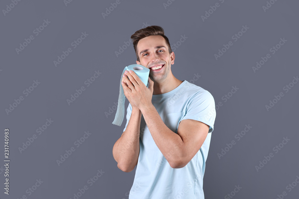 Young man holding toilet paper roll on color background Young man holding toilet paper roll on color background