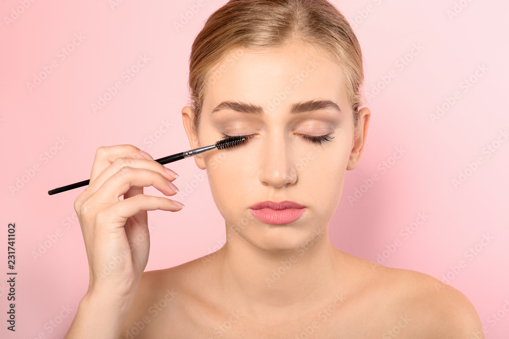 Portrait of young woman brushing her beautiful natural eyelashes on color background