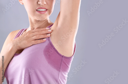 Young woman with sweat stain on her clothes against grey background, space for text. Using deodorant