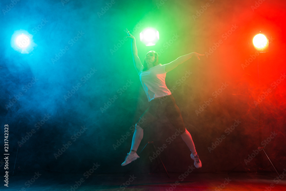 Dancing, sport, jazz funk and people concept - young woman jump in the darkness under colourful light