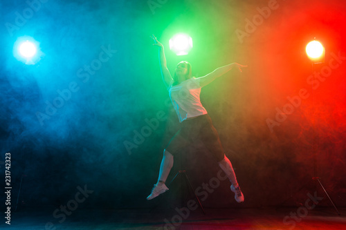 Dancing  sport  jazz funk and people concept - young woman jump in the darkness under colourful light