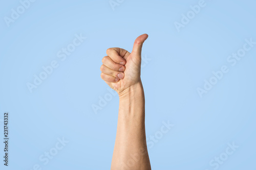 Male hand with a raised thumb on a blue background. Side picture. Gesture of approval, good work